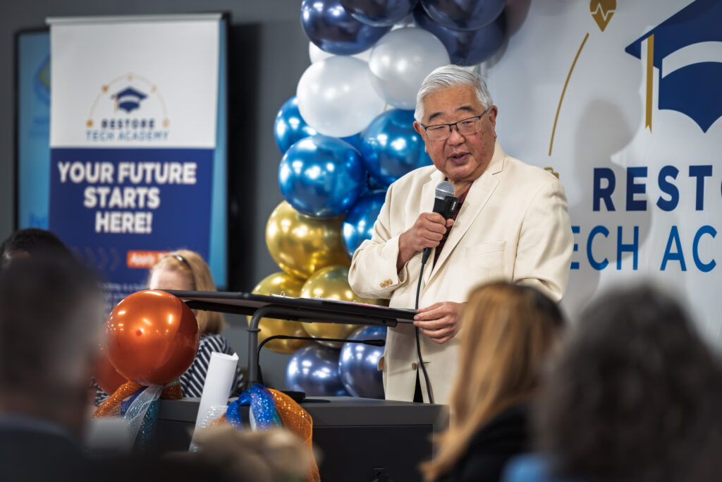 A speaker addresses attendees at the June 2026 Restore TECH Academy launch event, with a 'Your Future Starts Here' banner behind